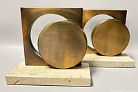 Front view of pair of brass-toned geometric sculptural bookends on light stone bases.