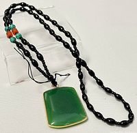 Front view of the jade pendant with bead necklace looped around a clear stand, showing detail of green jade and bead colors.