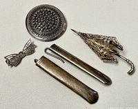 All five silver items shown together including brooches and other small objects, displayed on white fabric background