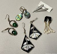 Photo showing all five pairs of sterling silver earrings with various stones and designs on a beige fabric background.