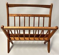 Front-facing view of the teak wood magazine rack showing the rectangular slatted storage compartment and curved top rail.