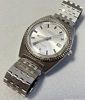 Front angle showing silver dial, hour markers, hands, date window, fluted bezel, and stainless steel bracelet.