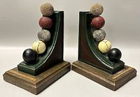 Pair of 'The Development of Balls' bookends showing five textured balls stacked vertically on curved green bases with wooden rectangular bases and gold plaque