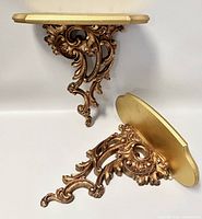 Pair of gold-tone wall sconces shown from angled perspective to highlight ornate design and shape.