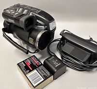 Panoramic view of the camcorder along with the power adaptor, battery case, and VHS tape, showing all items included in the lot.