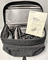 View inside carrying case showing cables, accessories, and instruction manual with Sony branding for DSR-PDX10 digital camcorder.