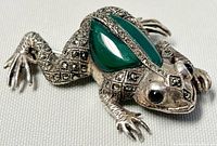 Close-up angle of frog brooch showing textured silver with marcasite stones and green stone inlays on back.