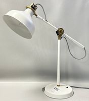 Full view of the white metal adjustable desk lamp with brass accents and braided power cord, showing the on/off switch on the base.