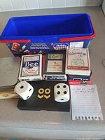Overview photo showing 6 decks of playing cards, 2 large white dice with black dots, one metal cribbage board, and a note listing contents
