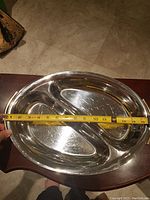 Oval divided stainless steel serving tray with measuring tape showing length of about 15 inches, placed on wooden surface