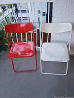 Red and white metal folding chairs made by IKEA, featuring tubular metal frames and curved backrests and seats.