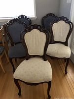 Six ornate dining chairs with carved wood frames; four blue upholstered and two cream upholstered chairs shown grouped together.