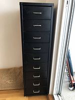 Front view of the tall black metal cabinet showing all eight drawers closed and metal handles.