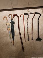 Photo of all items including two umbrellas with curved wooden handles and five walking canes of various designs and colors.