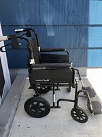 Side view of the Comfort Plus XC wheelchair showing black nylon seat, armrests, large rear wheels, anti-tip wheels, and foldable frame.