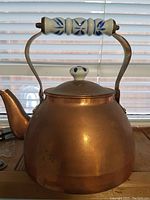 Front view of copper teapot with ceramic handle showing rounded body and lid knob. Photo taken to show overall item condition and ceramic detail.