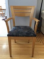 Front view of a wooden kitchen chair with arms and a patterned cushioned seat.