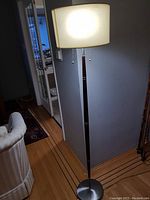 Photo of the standing floor lamp showing its brushed metal base, dark stem accents, and rectangular cream fabric shade lit up