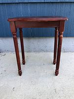 Full front view of the wooden side table showing a rectangular top with a curved front edge and four turned legs.
