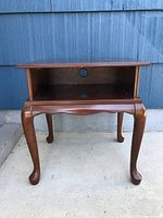 Front view of wooden side table displaying curved cabriole legs and open front storage with circular cable hole.