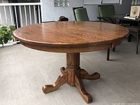 View of the full round solid oak dining table on a four-leg pedestal base with natural finish on an outdoor porch.