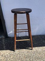 Full side view of the tall solid wood stool showing round seat and tapered legs with horizontal supports.
