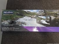 Full box front showing Revna brand tilting wall mount with scenic mountain and river background, product image of mount holding a flat TV.