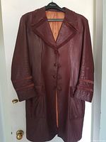 Full view of vintage men's burgundy leather coat with suede collar and cuffs, hanging on hanger against white door