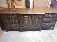 Front view of vintage wooden dresser showing six visible drawers and central double cabinet doors with decorative handles and keyholes.