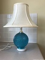 Full view of vintage blue glass lamp with white fabric shade and marble base on countertop
