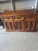 Front view of vintage wooden buffet cabinet showing three top drawers and two doors with carved decorative panels. Metal drawer handles.
