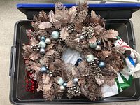 Vintage Christmas wreath with metallic bronze leaves, pinecones, and blue and silver decorative berries inside a plastic tub.