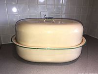Side view of vintage cream enamelware roasting pan with matching domed lid and green trim