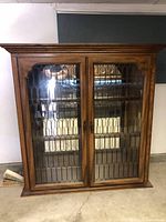 Full front view of the vintage wooden hutch cabinet showing two glass paneled doors with decorative metal grille and wooden frame.