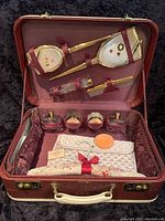 Open view of red vintage vanity suitcase showing all contents inside including glass bottles, mirror, brush, comb, clutch, and fabric piece.