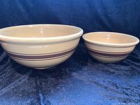 Front view of two ceramic mixing bowls side by side on blue velvet fabric background, showing their relative sizes and color pattern with brown stripes