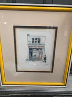 Framed watercolor print of a building facade labeled Palmistry Parlour with a figure walking by, signed by the artist. Yellow frame with cream mats.