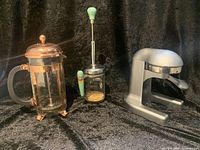 Full view of the three main items: Bodum copper coffee press, heavy metal juicer, antique nut grinder with wood handles and wood chopping token on black velvet background.