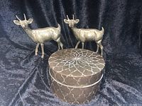 Brass cylindrical box with etched pattern and two brass roe deer figurines displayed behind it