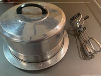 Photo showing cake carrier domed lid and base along with two vintage manual egg beaters with black handles