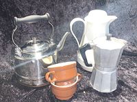 Full set including stainless steel tea kettle with copper bottom, white thermal carafe, brown speckled coffee cups, and stovetop espresso maker on black background.