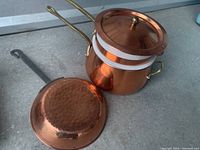 Shows copper ceramic double boiler pan with copper lid, white ceramic insert visible, and small hammered copper fry pan turned upside down showing texture on base with visible brass handles
