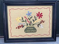 Full view of the framed crewel embroidered piece showing floral arrangement and embroidered text.