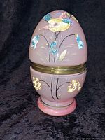 Closed view of pink painted glass egg-shaped decanter with bird and floral decorations and brass accents.