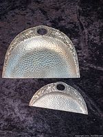 Front view of both hammered metal crumb trays showing embossed elephant motifs and round handles.
