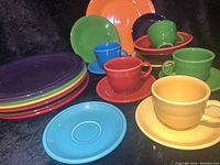 Set of Fiesta Ware dishes arranged showing cups on saucers, dinner and luncheon plates stacked, and bowls.