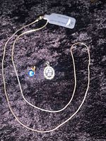 Sterling silver chain with two stone pendants on dark background, one blue stone pendant and one clear stone pendant with smaller surrounding stones.