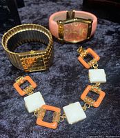 Three vintage Joan Rivers jewelry pieces placed on a black velvet surface, including a salmon and white bracelet, a gold tone expandable bracelet watch, and a pink hinged cuff watch.