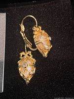 Close-up of Faberge Egg style Joan Rivers earrings showing intricate lattice gold-tone metal design with opalescent and iridescent rhinestones, bow detail at the top.