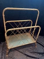 Front and side view of gold tone magazine rack showing bamboo style tubular frame and caned mesh bottom